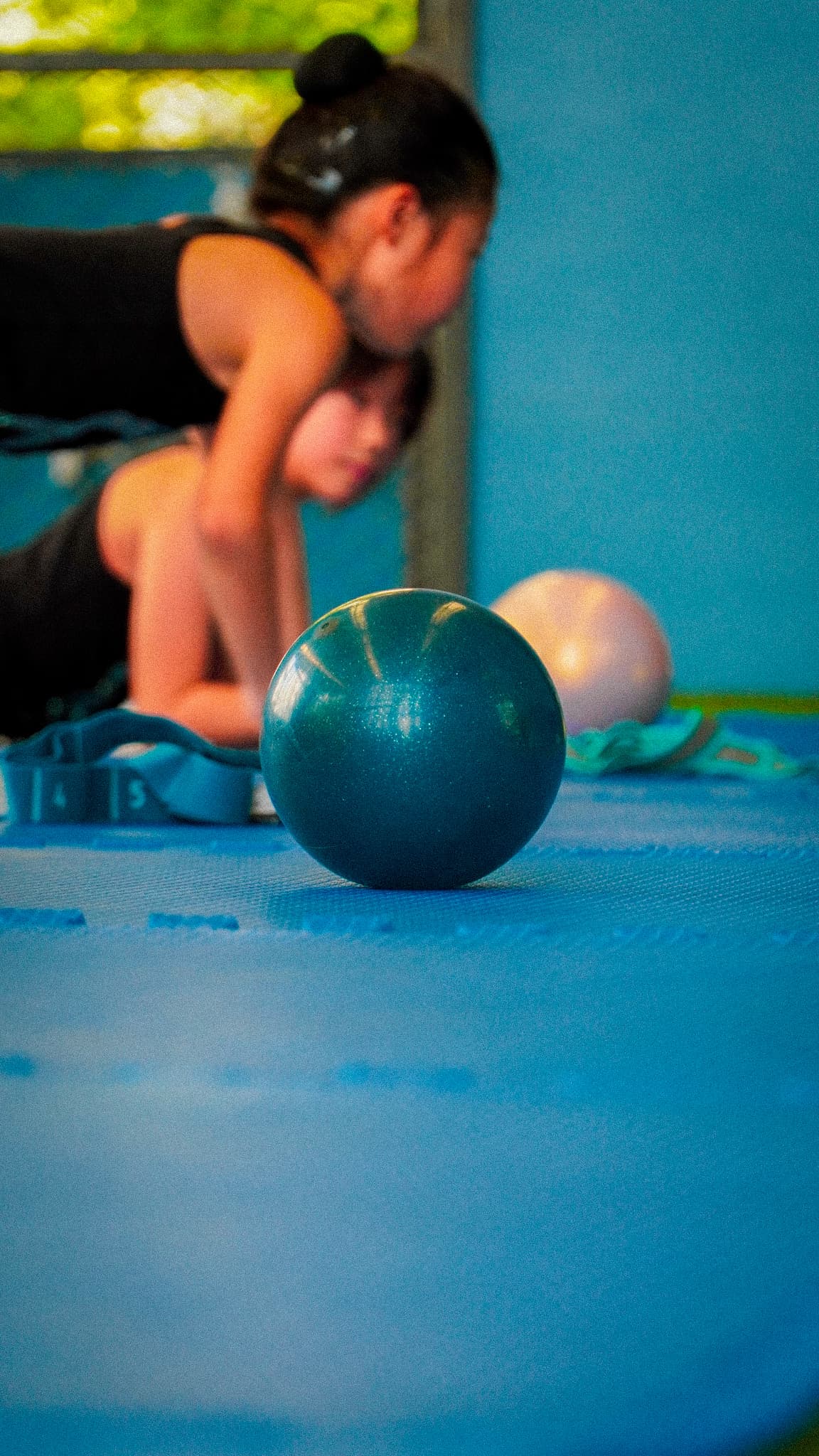 Rhythmic gymnastics ball on the mat with coach in background